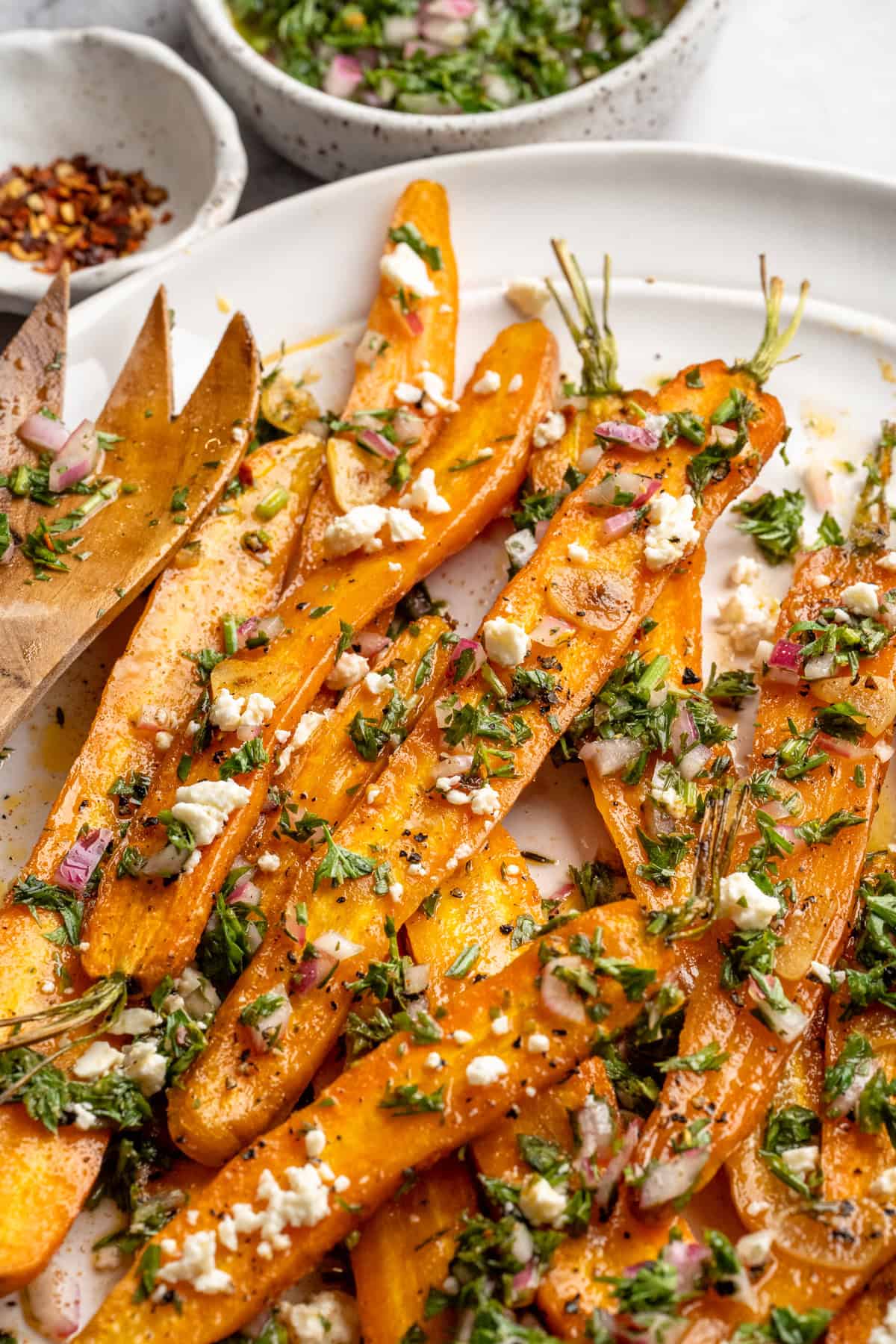 These perfectly caramelized maple roasted carrots are served with a vibrant chimichurri made from the carrot greens themselves. A plate of maple roasted carrots topped with vegan feta and carrot top chimichurri.