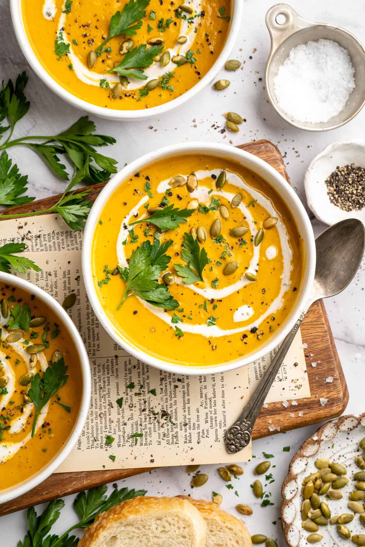 Bowls of roasted sweet potato soup garnished with coconut milk, pumpkin seeds, and parsley.