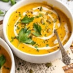 A bowl of sweet potato soup garnished with coconut milk, pumpkin seeds, and parsley.