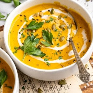 A bowl of sweet potato soup garnished with coconut milk, pumpkin seeds, and parsley.