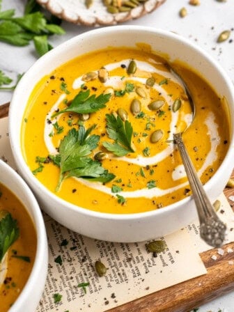 A bowl of sweet potato soup garnished with coconut milk, pumpkin seeds, and parsley.