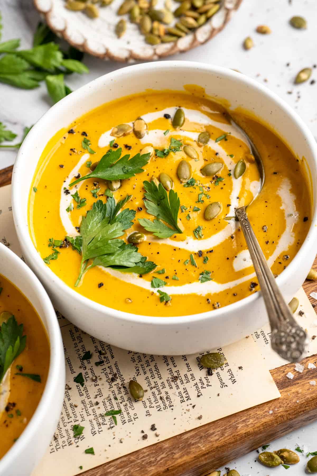 A bowl of sweet potato soup garnished with coconut milk, pumpkin seeds, and parsley.