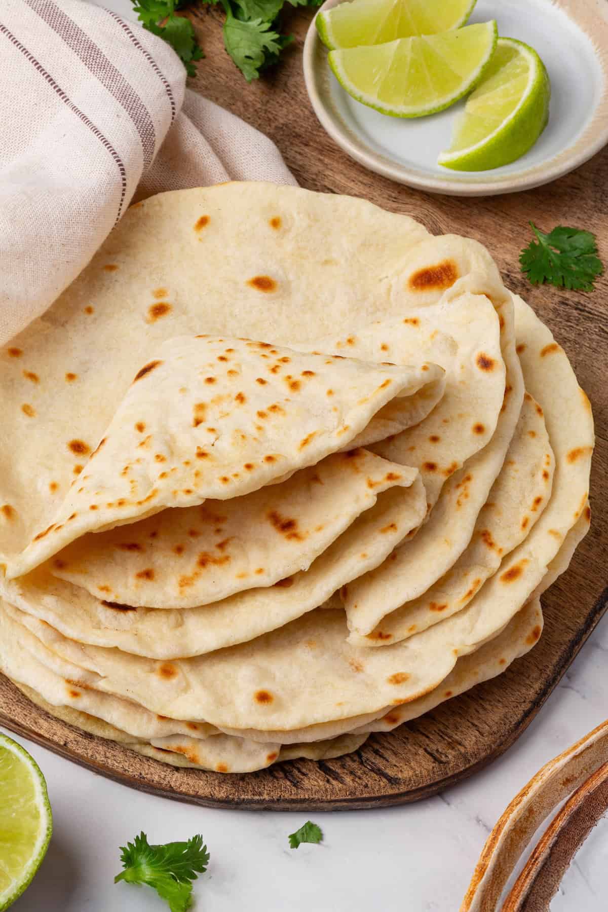 Perfectly soft and chewy, these homemade vegan flour tortillas puff up beautifully in the pan and are ideal for your next burrito. A stack of vegan flour tortillas with several folded on top.