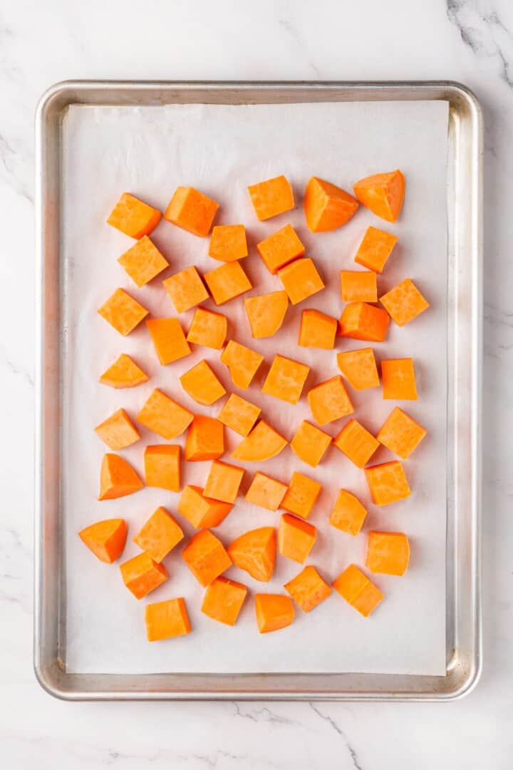 This sweet 'n savoury sweet potato salad is full of warm, tender sweet potatoes, crisp, peppery arugula, toasted pecans, and tangy vegan feta. Cubed sweet potato spread out on a baking sheet.