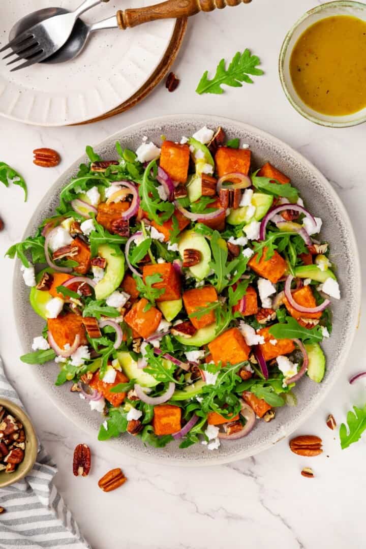 This sweet 'n savoury sweet potato salad is full of warm, tender sweet potatoes, crisp, peppery arugula, toasted pecans, and tangy vegan feta. Overhead image of sweet potato arugula salad with maple-Dijon dressing.
