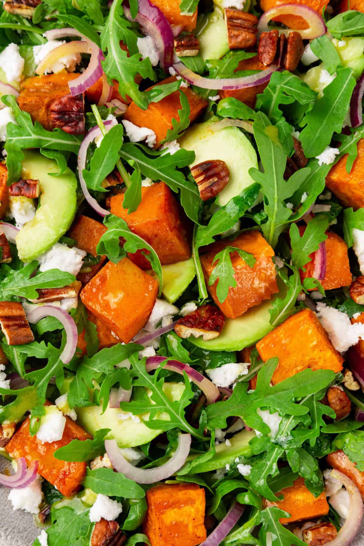 This sweet 'n savoury sweet potato salad is full of warm, tender sweet potatoes, crisp, peppery arugula, toasted pecans, and tangy vegan feta. Closeup image of sweet potato arugula salad with maple-Dijon dressing.