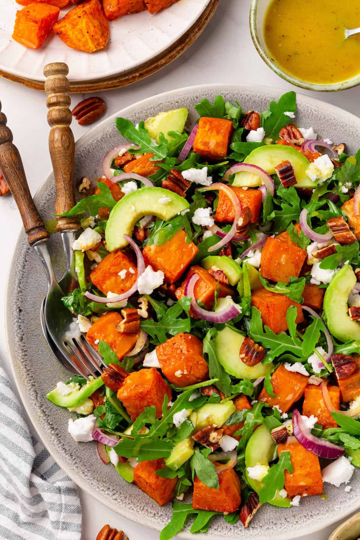This sweet 'n savoury sweet potato salad is full of warm, tender sweet potatoes, crisp, peppery arugula, toasted pecans, and tangy vegan feta. Overhead image of sweet potato arugula salad on a serving platter.