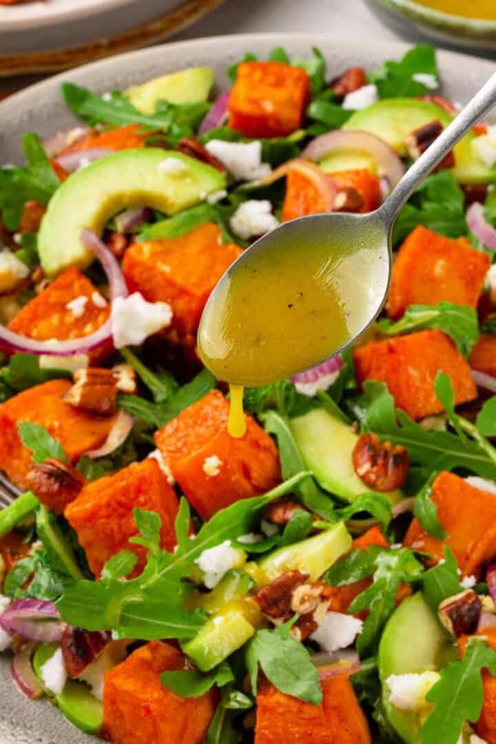 This sweet 'n savoury sweet potato salad is full of warm, tender sweet potatoes, crisp, peppery arugula, toasted pecans, and tangy vegan feta. Spooning lemony maple-Dijon dressing over roasted sweet potato arugula salad.