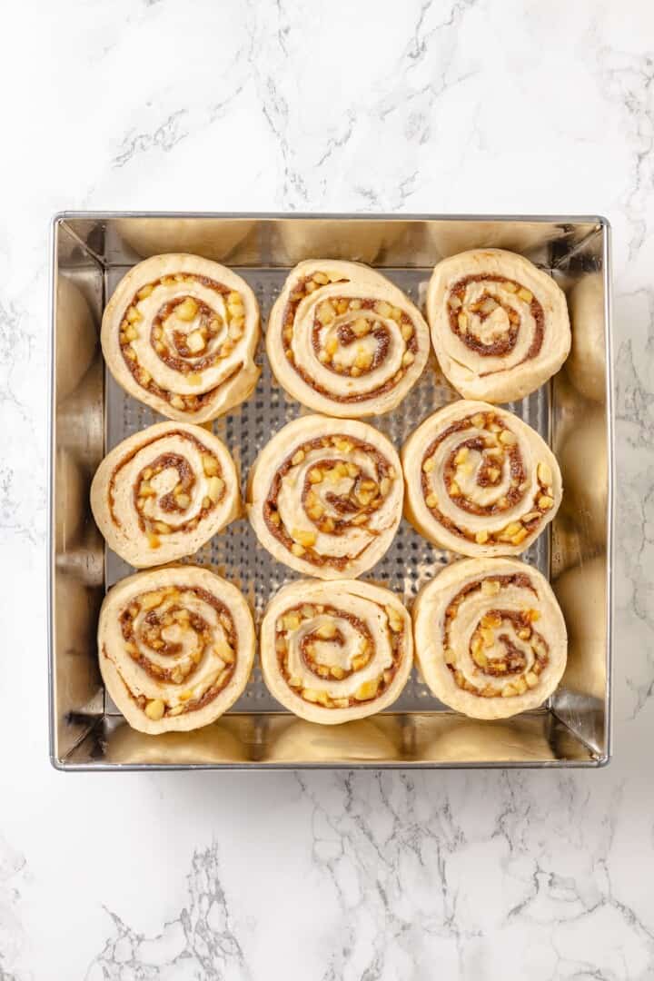 Fabulously fluffy, filled with soft, cinnamony apples, and topped with cream cheese frosting, you need these apple cinnamon rolls now. Unbaked apple cinnamon rolls arranged in a pan to rise.