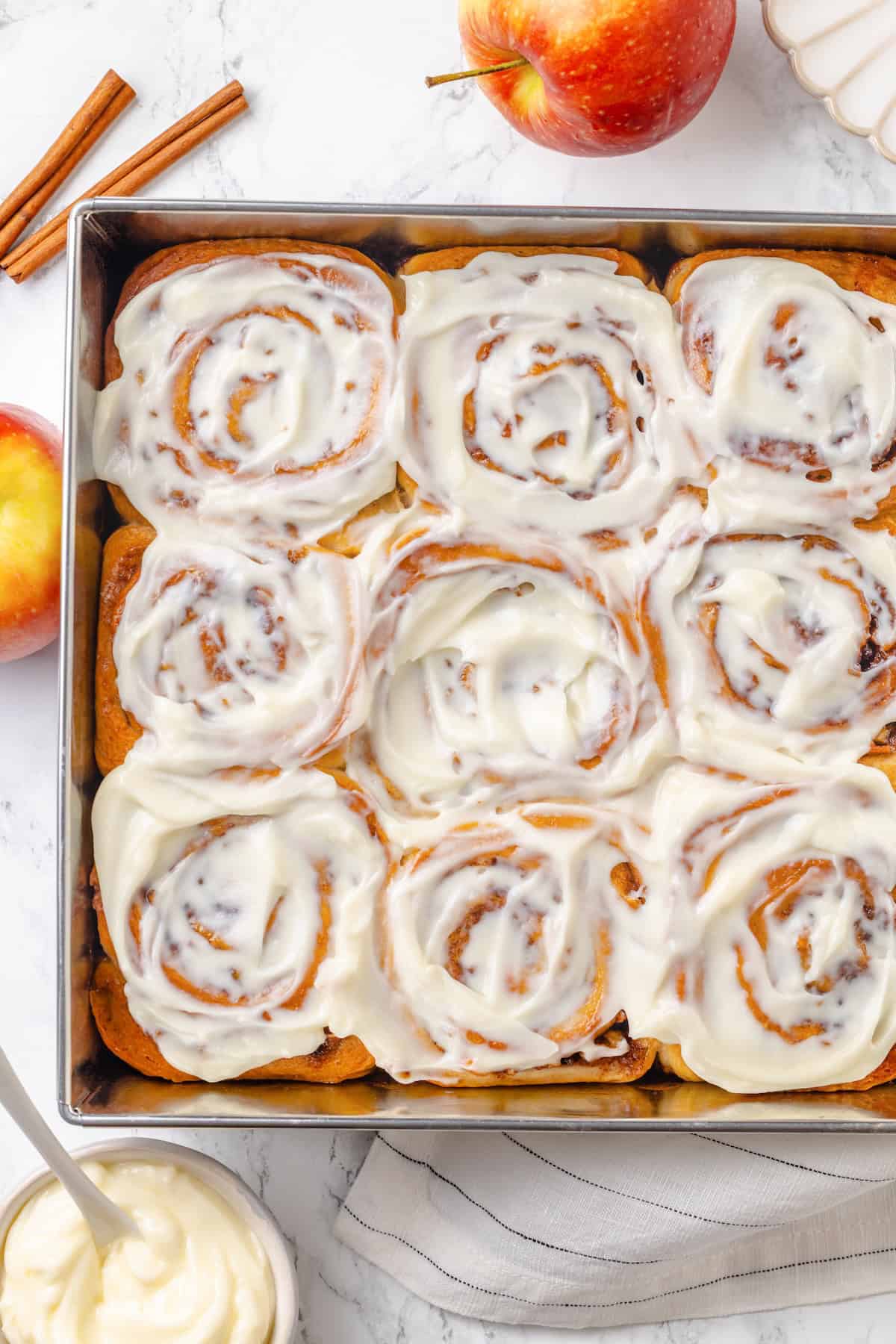 Fabulously fluffy, filled with soft, cinnamony apples, and topped with cream cheese frosting, you need these apple cinnamon rolls now. Overhead image of a baking pan full of vegan apple pie cinnamon rolls.