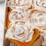 A spatula lifting a vegan apple cinnamon roll out of a baking pan.