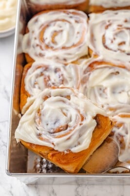 A spatula lifting a vegan apple cinnamon roll out of a baking pan.