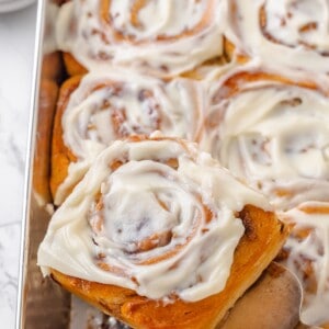 A spatula lifting a vegan apple cinnamon roll out of a baking pan.