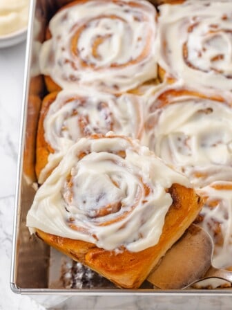 A spatula lifting a vegan apple cinnamon roll out of a baking pan.