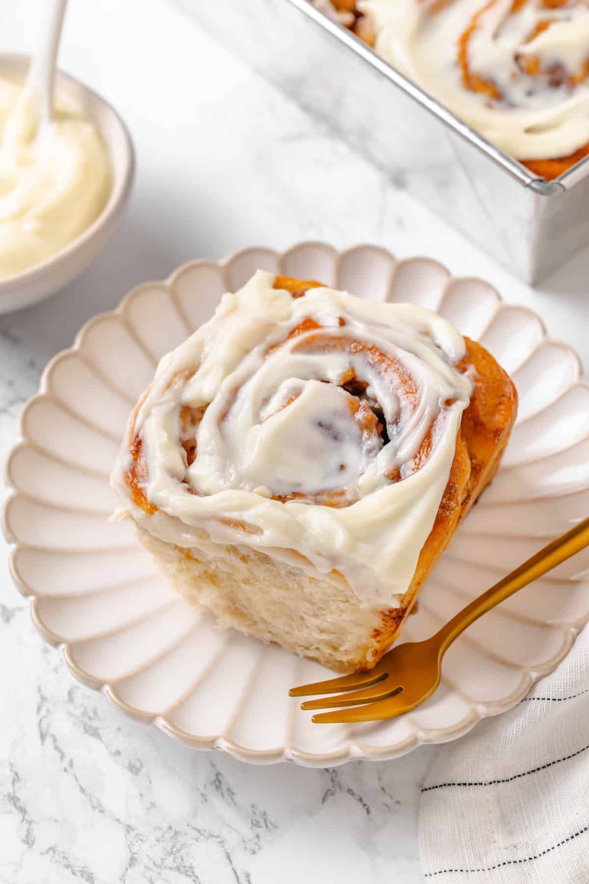 Fabulously fluffy, filled with soft, cinnamony apples, and topped with cream cheese frosting, you need these apple cinnamon rolls now. A vegan apple cinnamon roll on a plate with a fork.