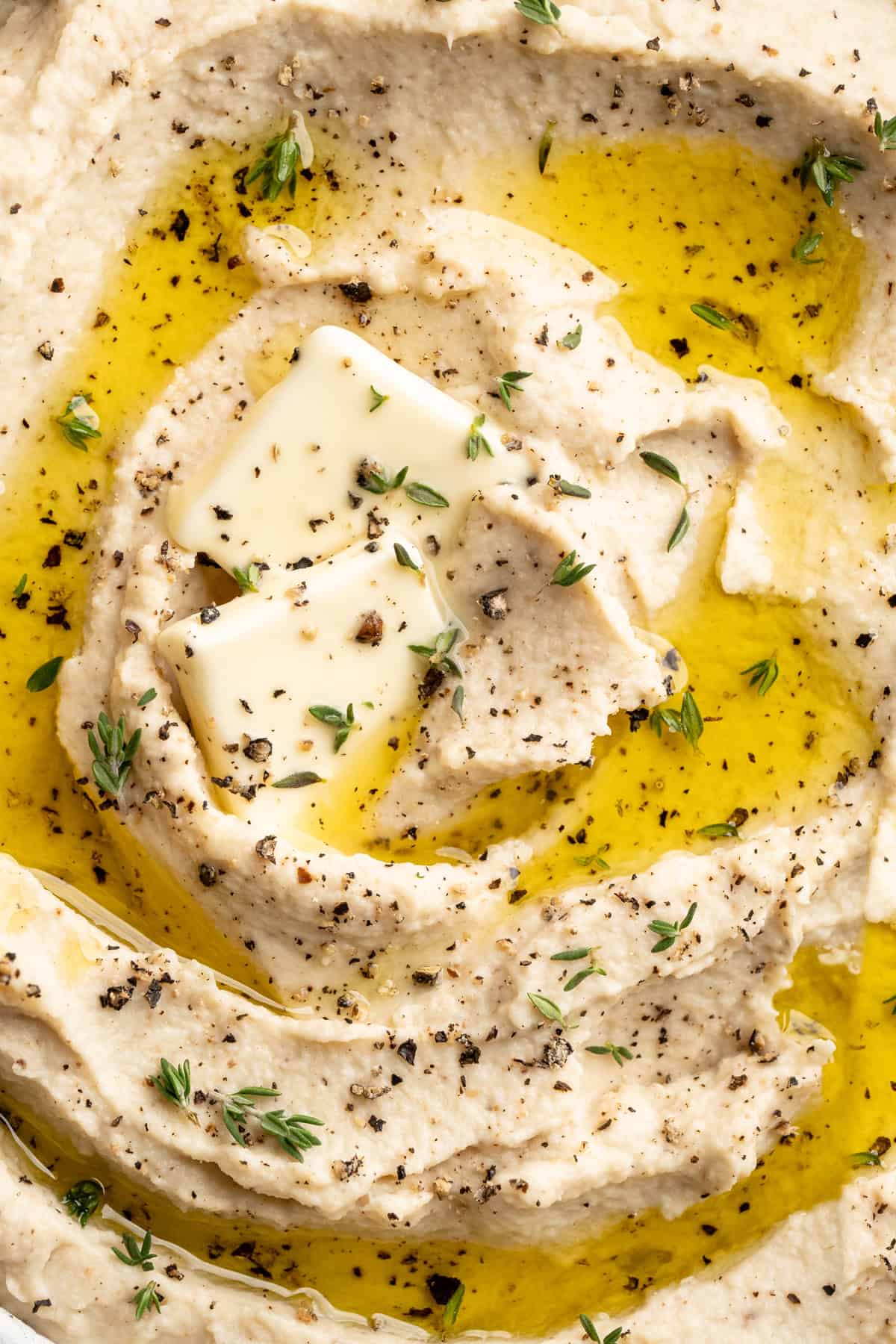 This cauliflower mash is made with roasted cauliflower and garlic for the ultimate sauvoury flavour, and coconut milk for a silky finish. Closeup image of vegan mashed cauliflower topped with olive oil and vegan butter.