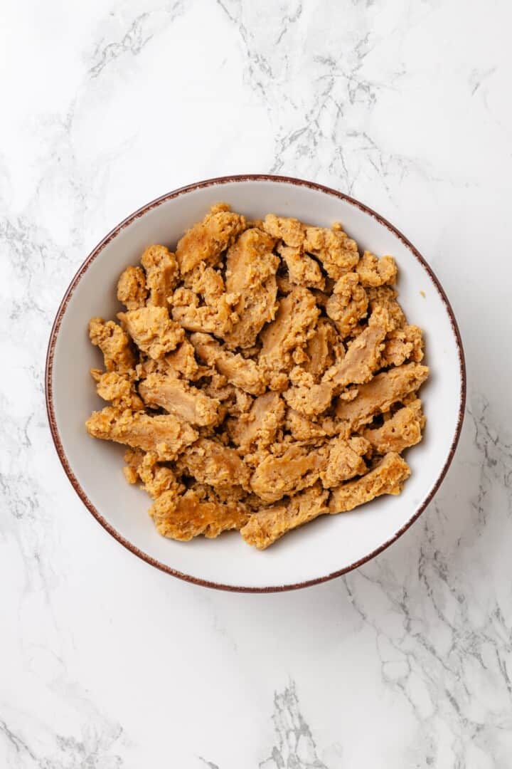 This vegan Philly cheesesteak is piled high with golden-brown, savoury soy curl "steak", tender sautéed veggies, and melted vegan provolone. Drained and squeezed soy curls in a bowl.