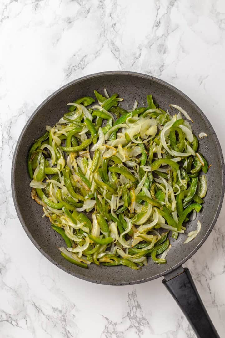 This vegan Philly cheesesteak is piled high with golden-brown, savoury soy curl "steak", tender sautéed veggies, and melted vegan provolone. Sautéed onion and green bell pepper in a skillet.