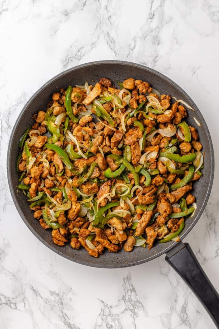 This vegan Philly cheesesteak is piled high with golden-brown, savoury soy curl "steak", tender sautéed veggies, and melted vegan provolone. A skillet full of sautéed veggies and golden-brown soy curl "steak" bites.
