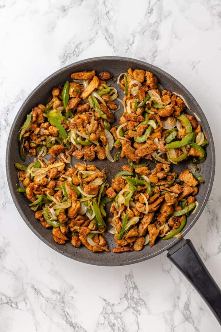 This vegan Philly cheesesteak is piled high with golden-brown, savoury soy curl "steak", tender sautéed veggies, and melted vegan provolone. Vegan Philly cheesesteak filling divided into four portions in a pan.
