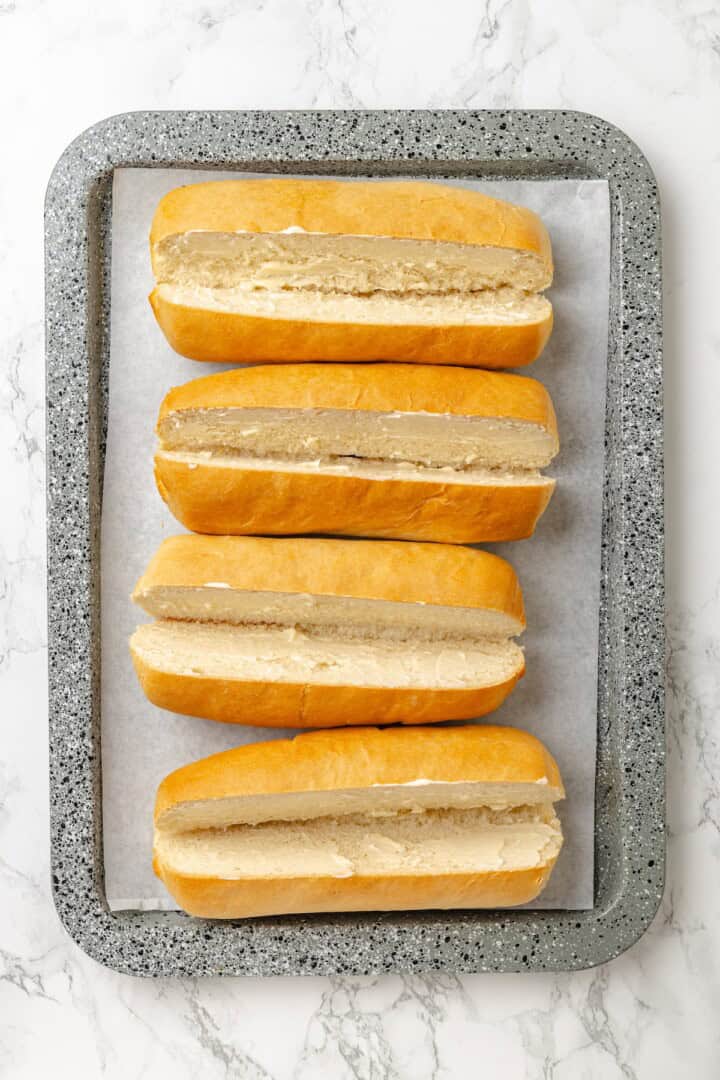 This vegan Philly cheesesteak is piled high with golden-brown, savoury soy curl "steak", tender sautéed veggies, and melted vegan provolone. Halved and buttered hoagie rolls on a sheet pan.
