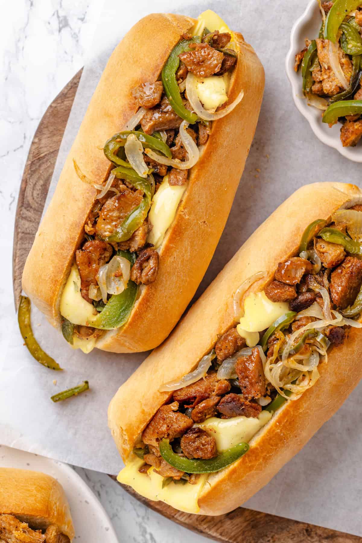 This vegan Philly cheesesteak is piled high with golden-brown, savoury soy curl "steak", tender sautéed veggies, and melted vegan provolone. Overhead image of soy curl Philly cheesesteaks in buttered, toasted hoagie rolls.
