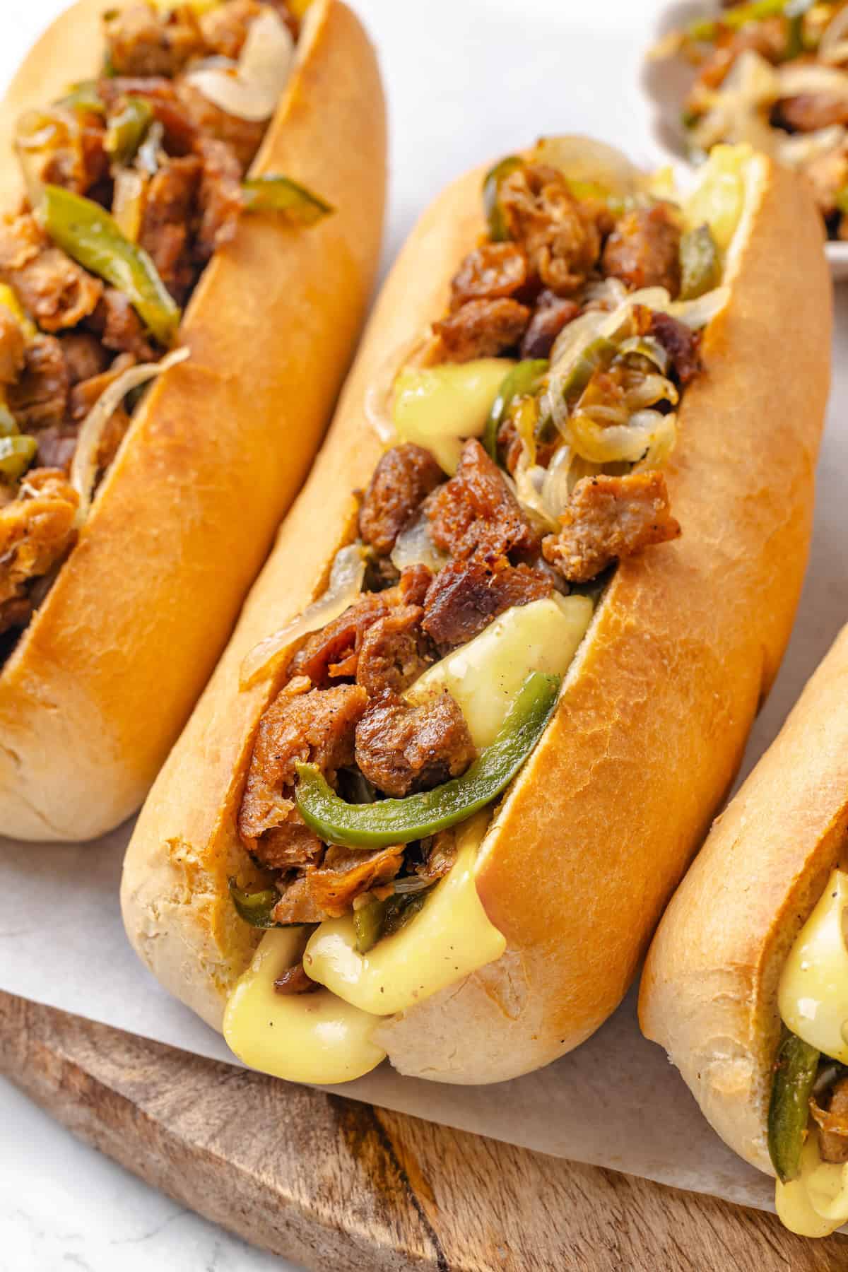 This vegan Philly cheesesteak is piled high with golden-brown, savoury soy curl "steak", tender sautéed veggies, and melted vegan provolone. Soy curl Philly cheesesteak sandwiches lined up in a row.