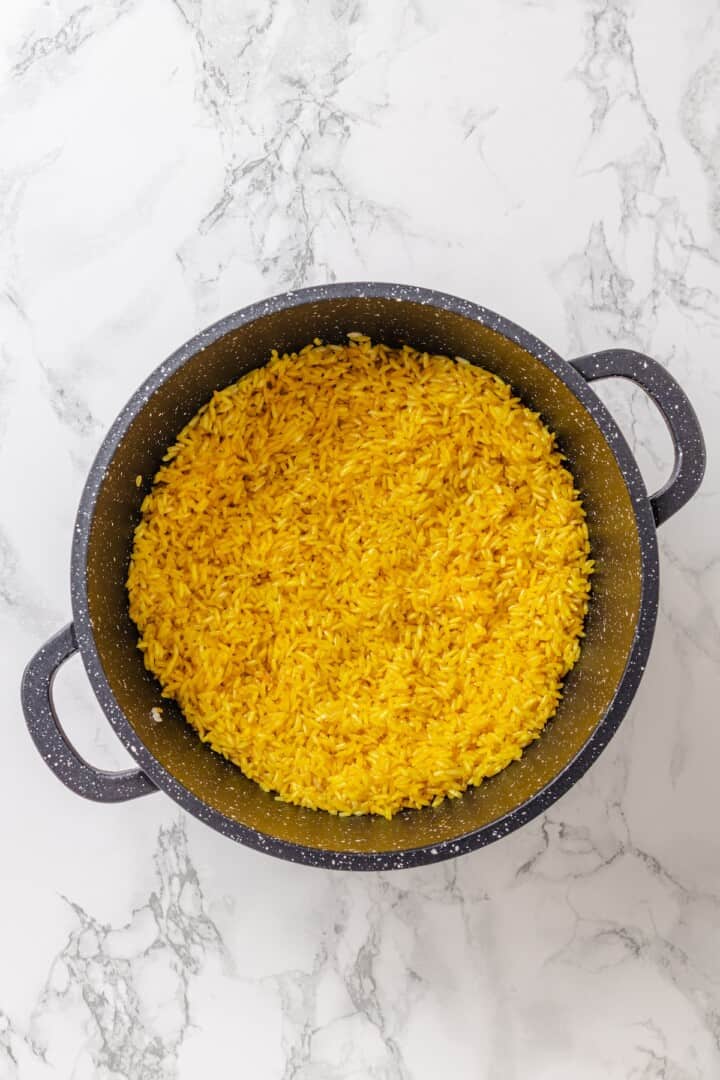 This easy yellow rice is toasted with peppery turmeric and warming cumin and simmered to fluffy perfection in veggie broth. Toasting cumin, turmeric, and garlic powder in a saucepan with toasted rice.