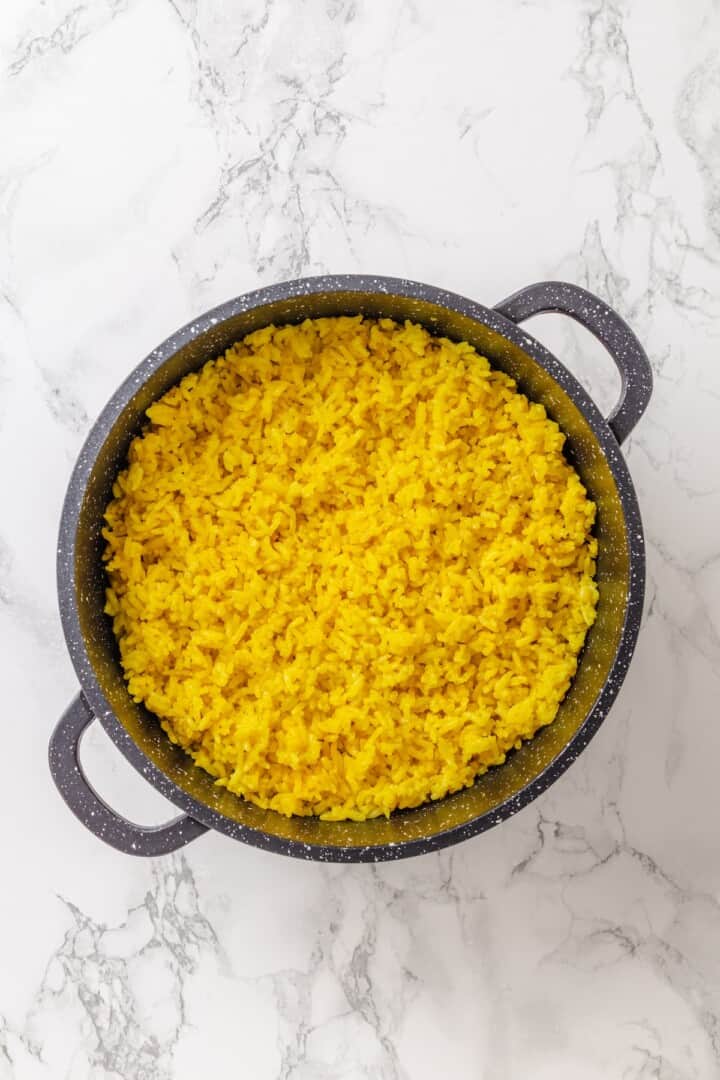 This easy yellow rice is toasted with peppery turmeric and warming cumin and simmered to fluffy perfection in veggie broth. Fluffed up vegan yellow rice in a saucepan.