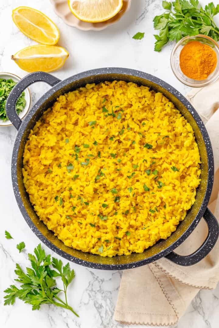 This easy yellow rice is toasted with peppery turmeric and warming cumin and simmered to fluffy perfection in veggie broth. A saucepan full of fluffy vegan yellow rice garnished with fresh parsley.