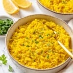 A bowl of fluffy vegan yellow rice garnished with fresh parsley.