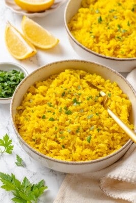 A bowl of fluffy vegan yellow rice garnished with fresh parsley.