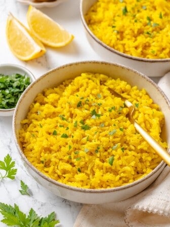 A bowl of fluffy vegan yellow rice garnished with fresh parsley.