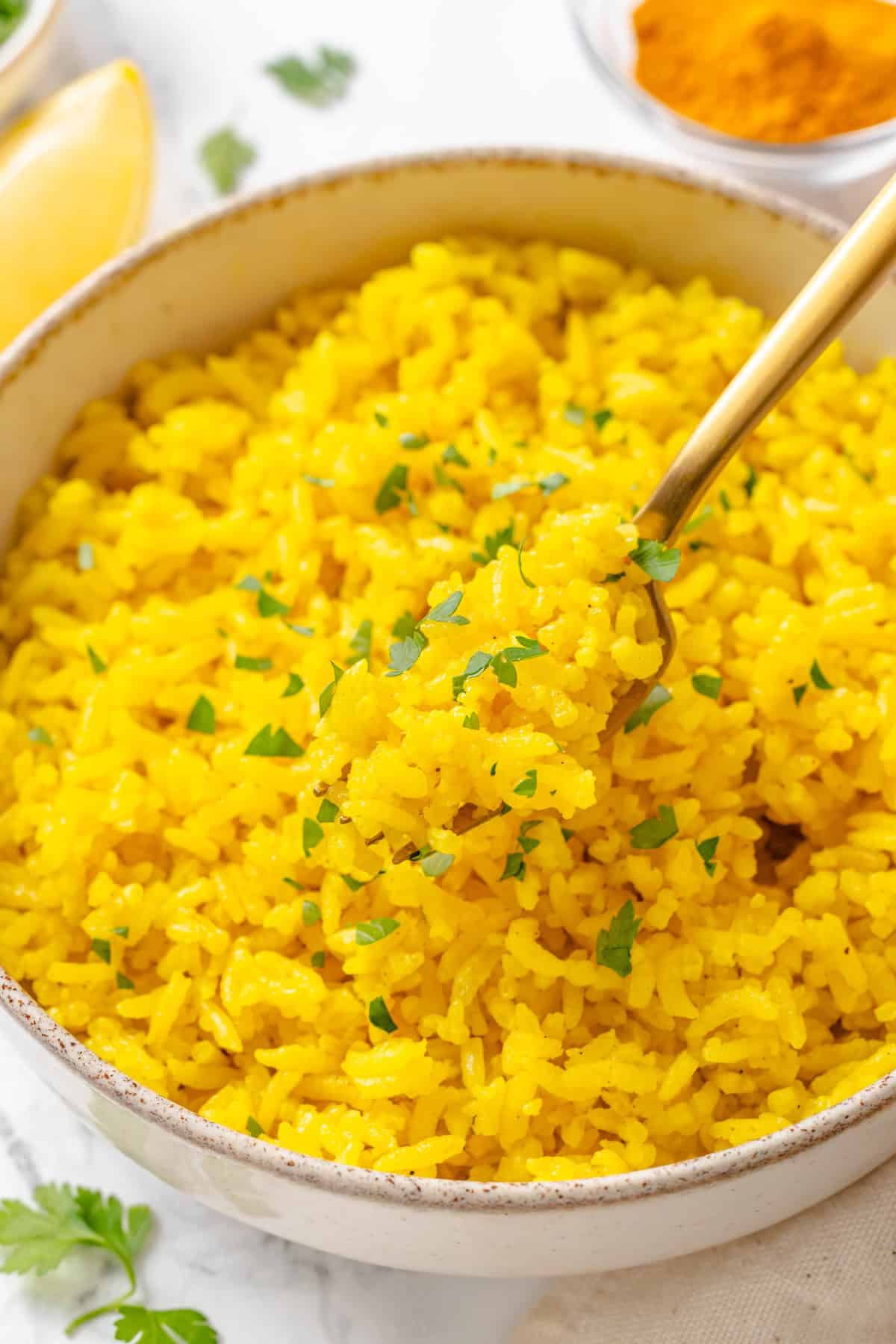 This easy yellow rice is toasted with peppery turmeric and warming cumin and simmered to fluffy perfection in veggie broth. A fork diving into a bowl of fluffy vegan yellow rice.